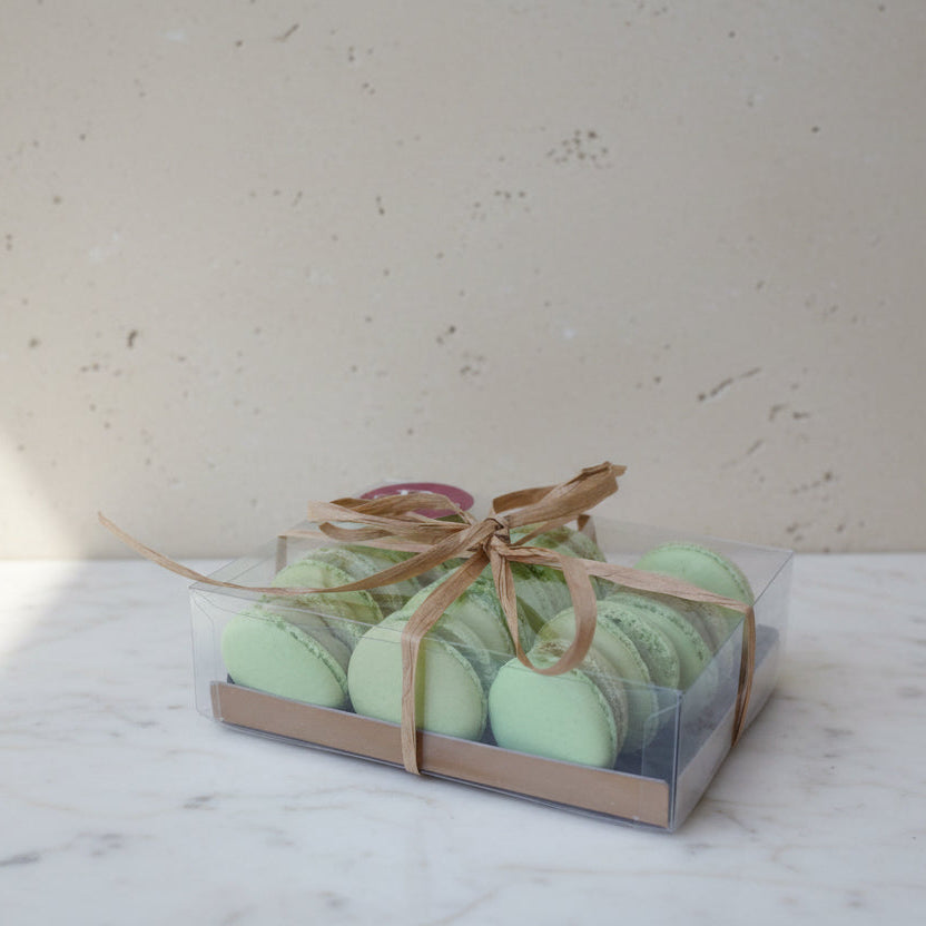 A gift box of light green macarons tied with a brown ribbon, placed on a wooden slatted table.