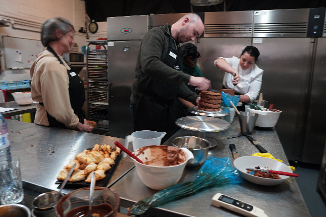 People working in a kitchen preparing food with various utensils and ingredients.