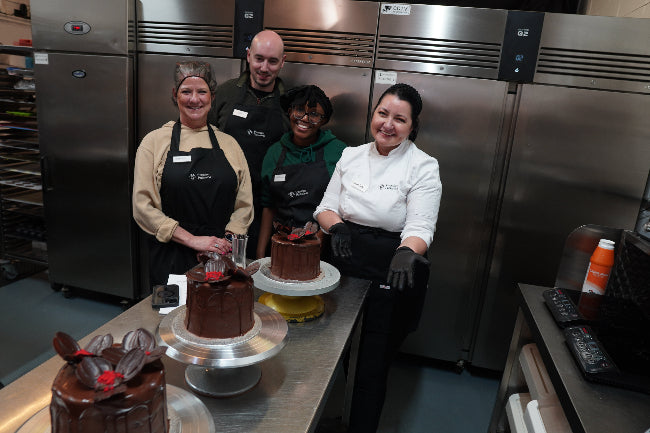 Four chefs posing with chocolate cakes in a kitchen setting