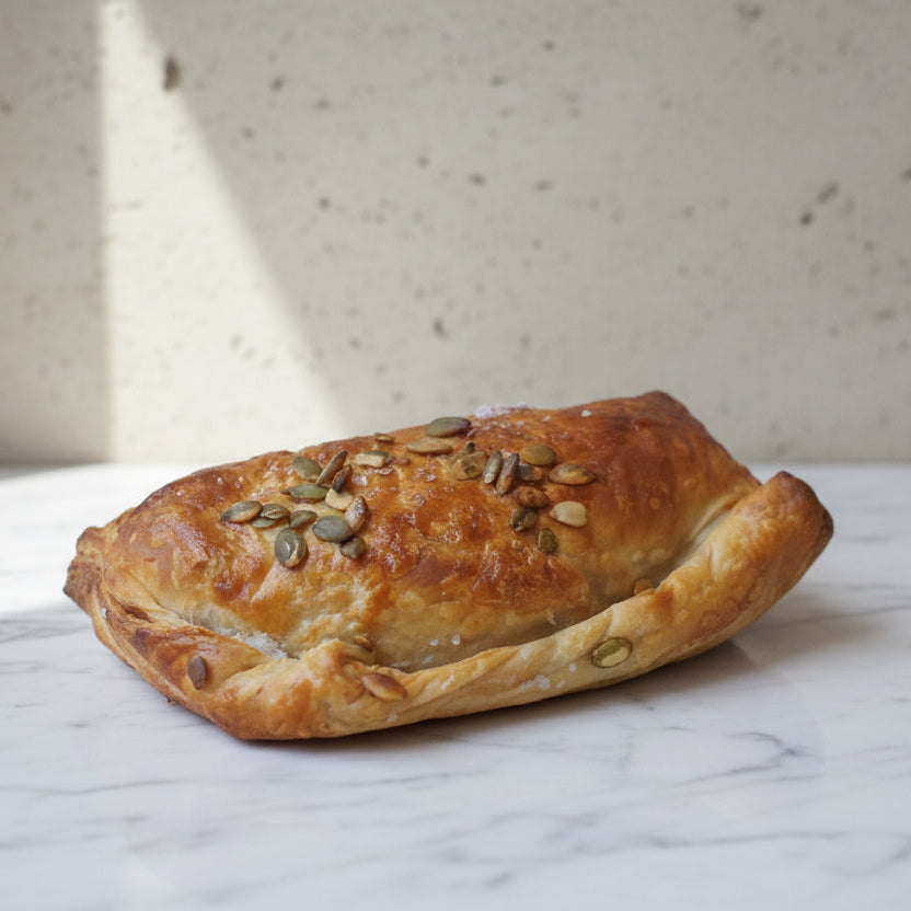 A pastie with a flaky, buttery shortcrust pastry topped with roasted butternut squash, onion, and goat cheese, garnished with pumpkin seeds.