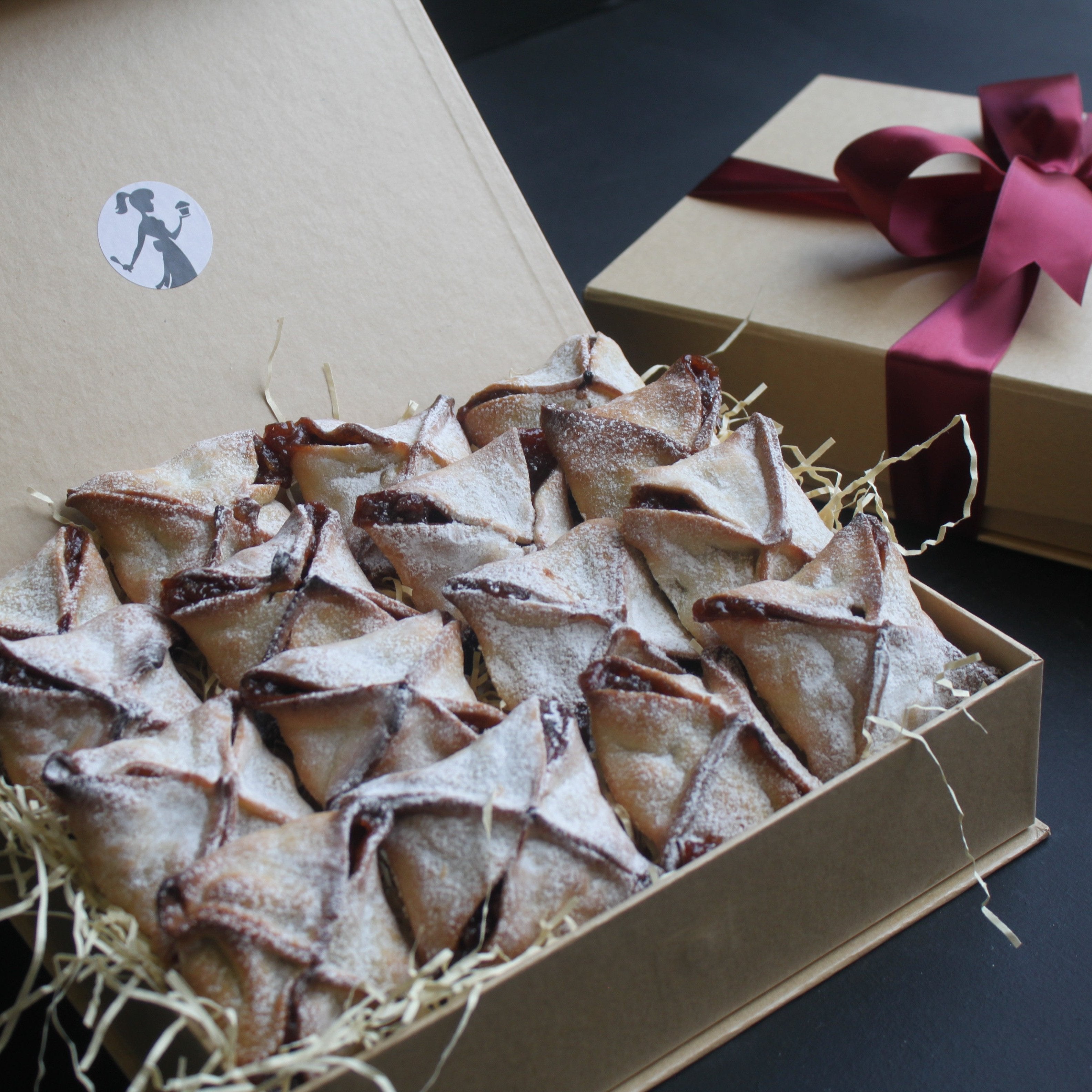 A small gift box open to reveal multiple mince pies arranged in it, with a decorative bow on the top.