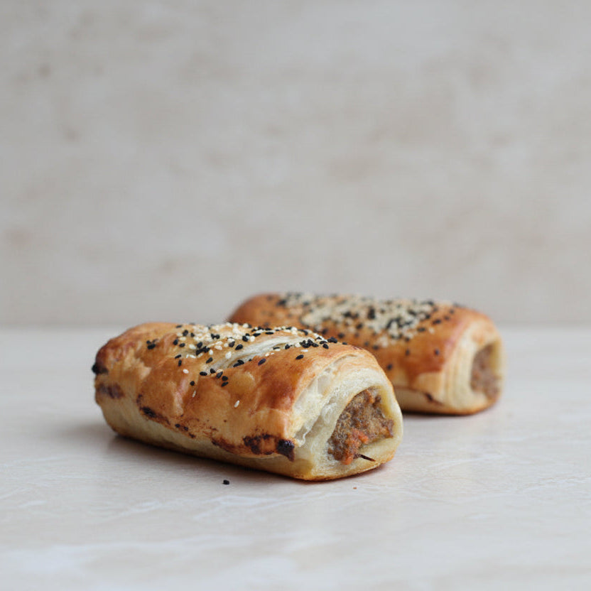 Handmade pork and beef sausage rolls in flaky puff pastry topped with sesame and Nigella seeds, baked golden brown in North London bakery